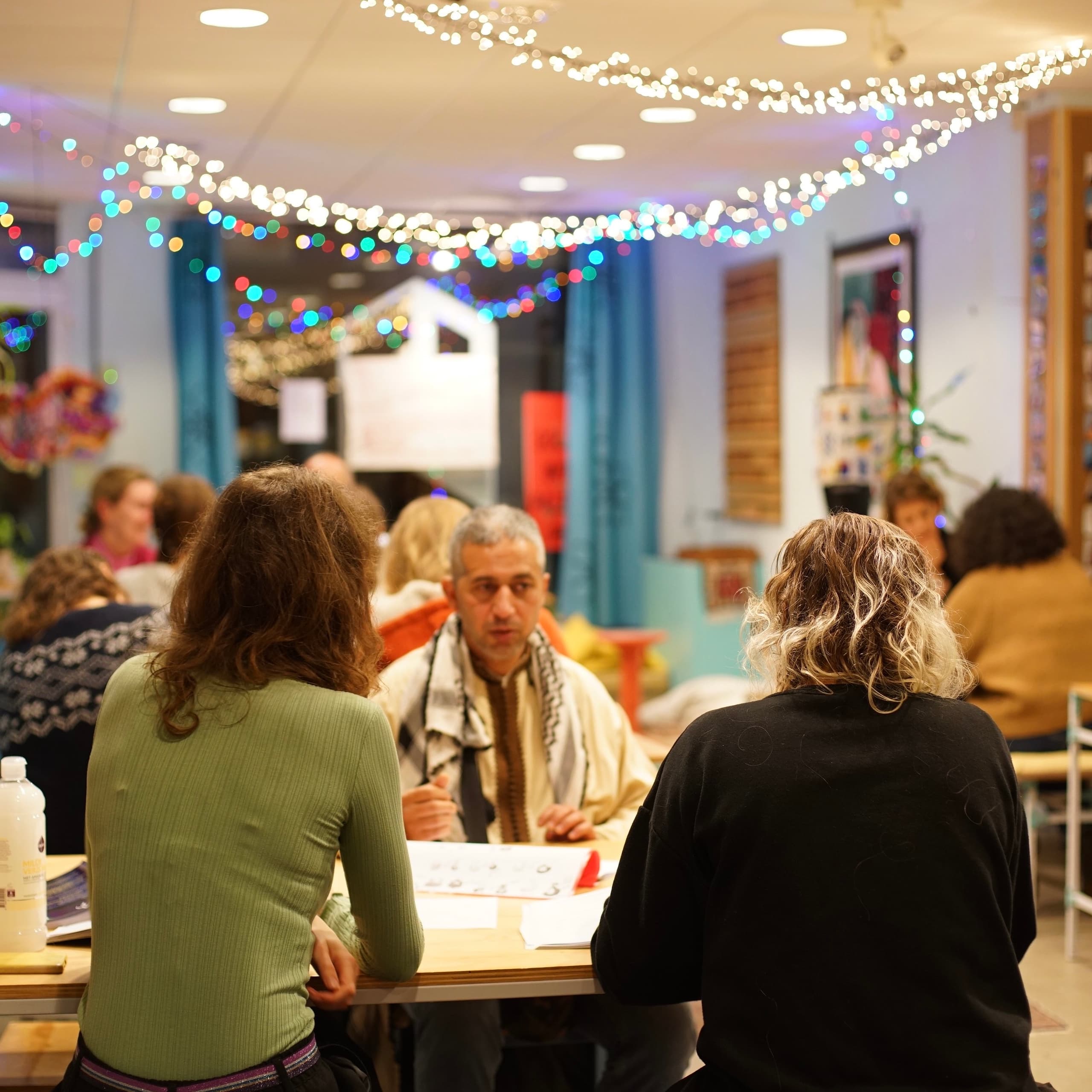 Participants in conversation at tables under strings of fairy lights during the Arabic Language Café.
