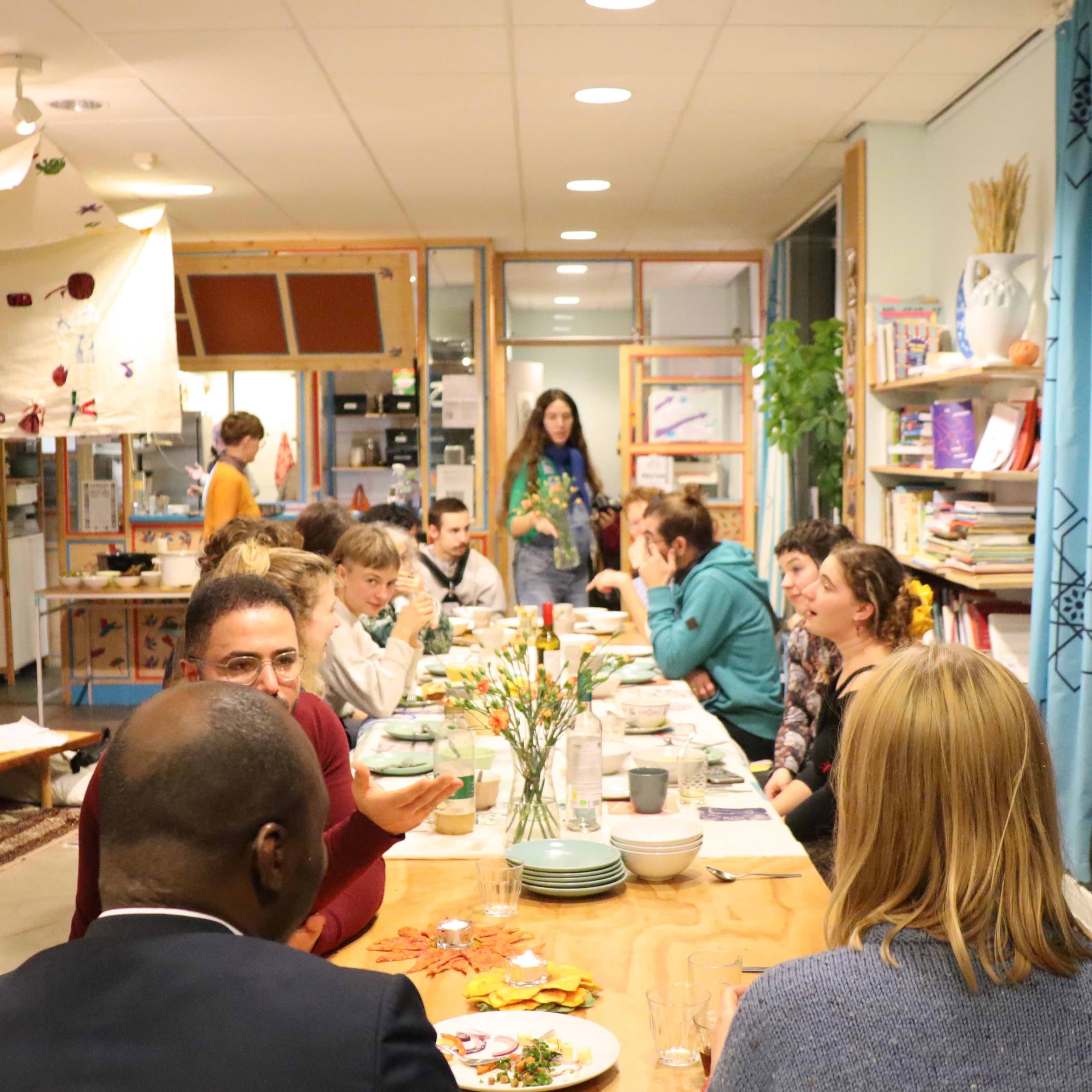 Guests eating together at a long table set with flowers during a Community Dinner.