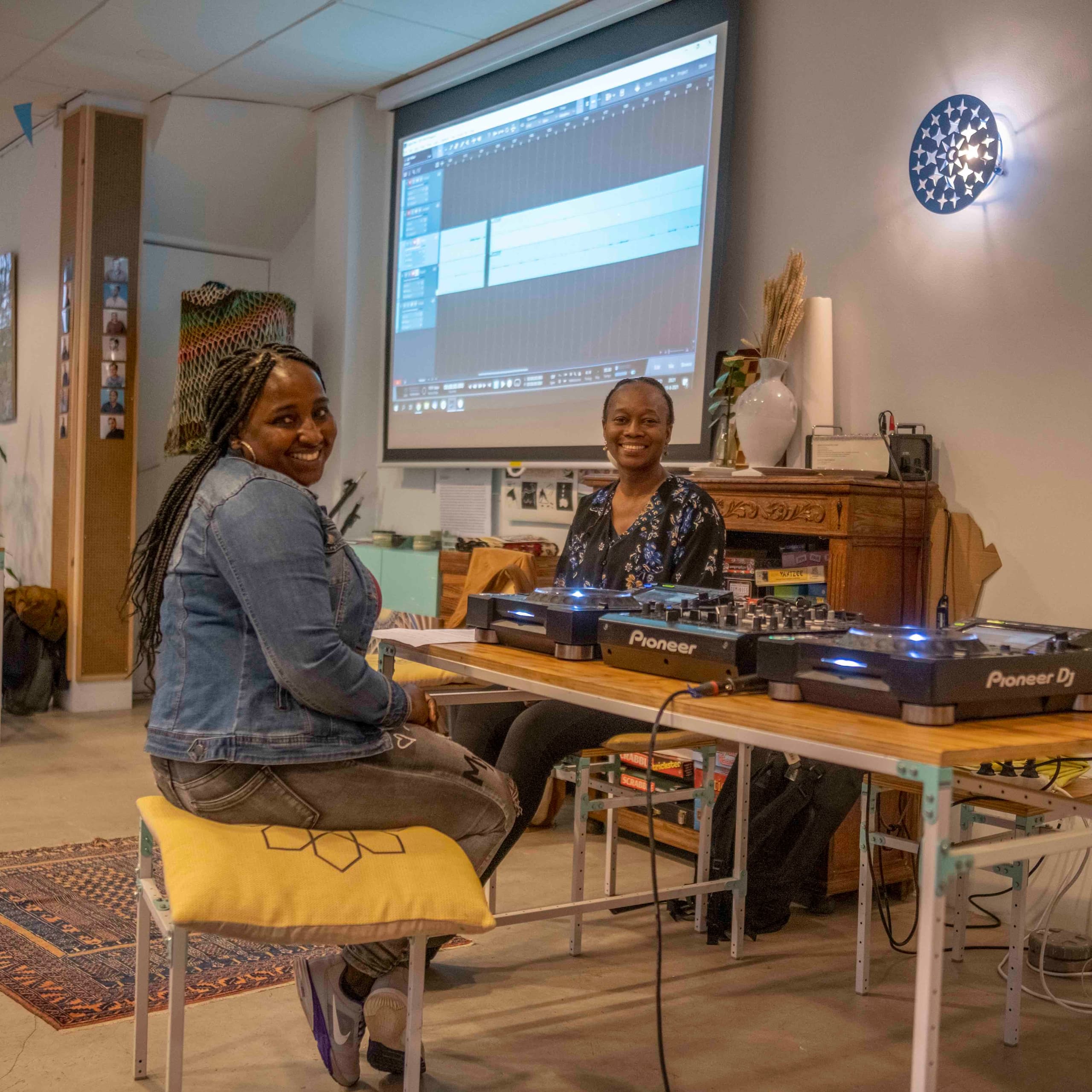 Two participants at the mixing desk in front of a projection screen during the radio-making course.