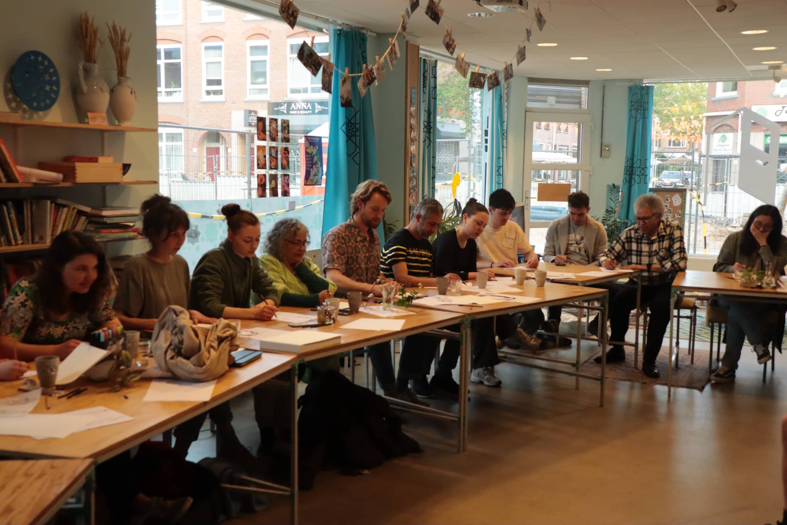 Participants writing together at long wooden tables in De Voorkamer's window-lit main room during a workshop.