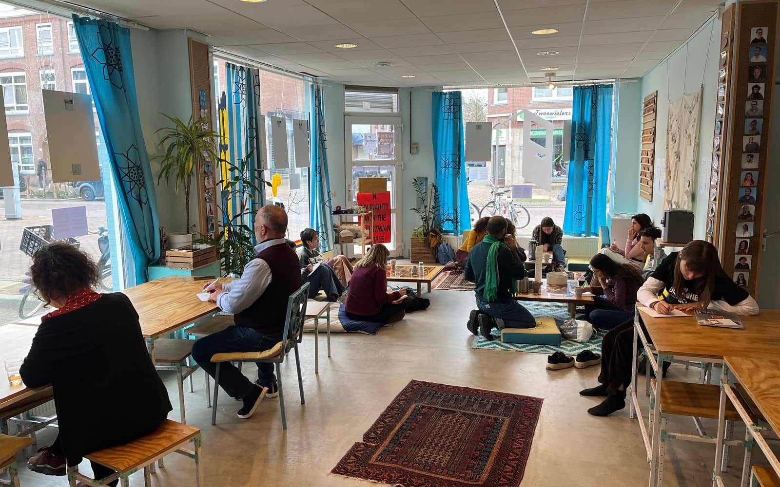 People working at tables and sitting on rugs in the main room during Community Open Hours.