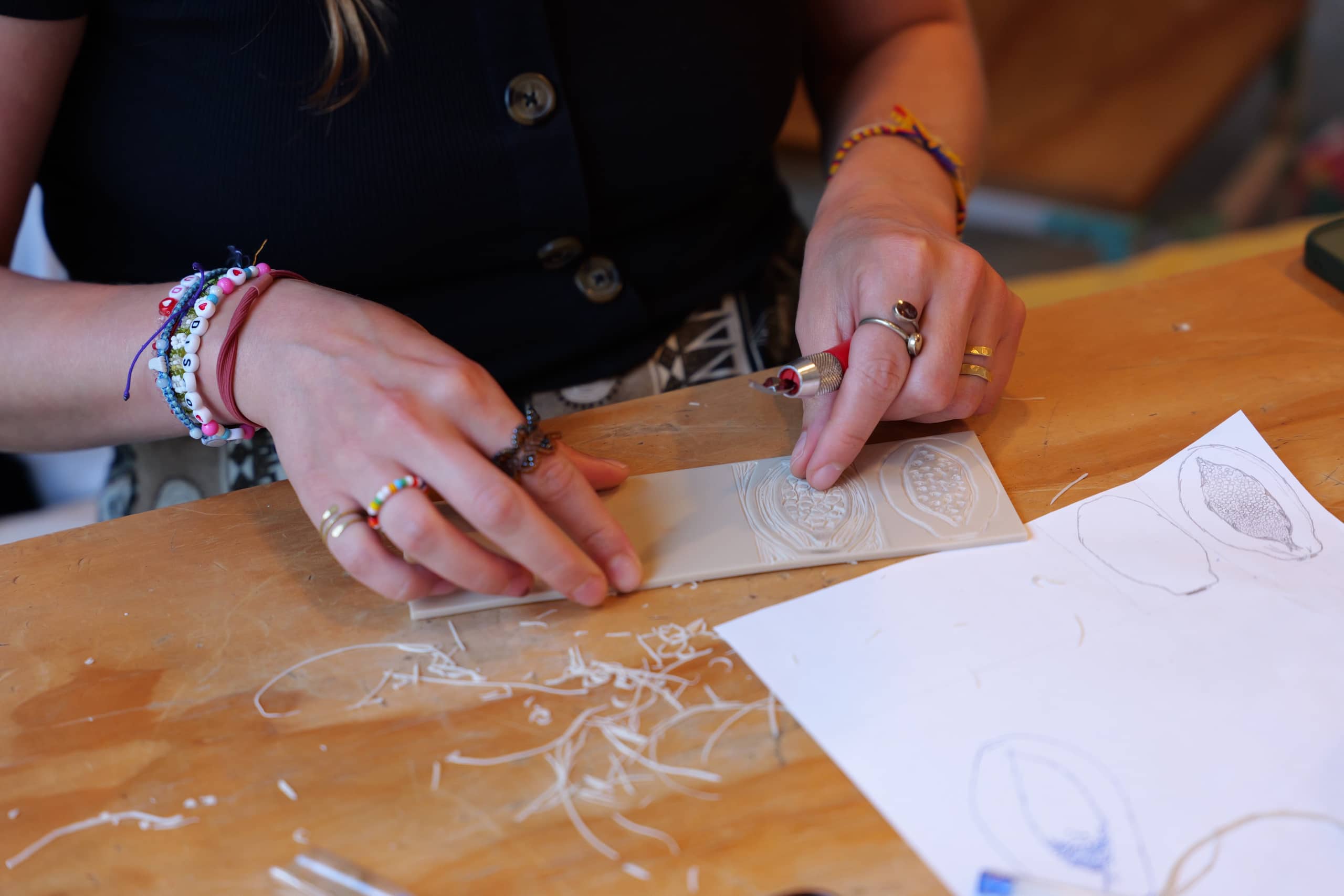 Hands carving a lino block beside pencil sketches during the Lino Group.